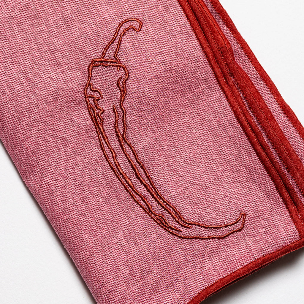 Pink fabric with embroidered chili pepper design on a white background