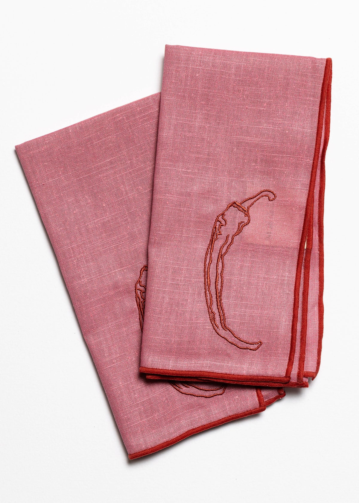 Two pink napkins with embroidered chili pepper design on a white background