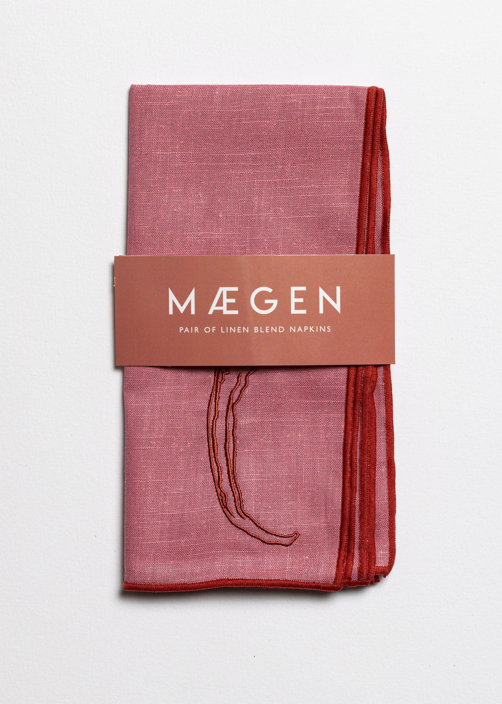 Packaged pink linen blend napkins with 'Máegen' branding on a light gray background