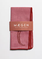Packaged pink linen blend napkins with 'Máegen' branding on a light gray background